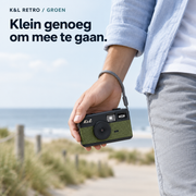 Groene K&L Retro Camera met grijze polsband in de hand, onderweg aan zee.