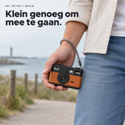 Bruine K&L Retro Camera met grijze polsband in de hand, onderweg aan zee.