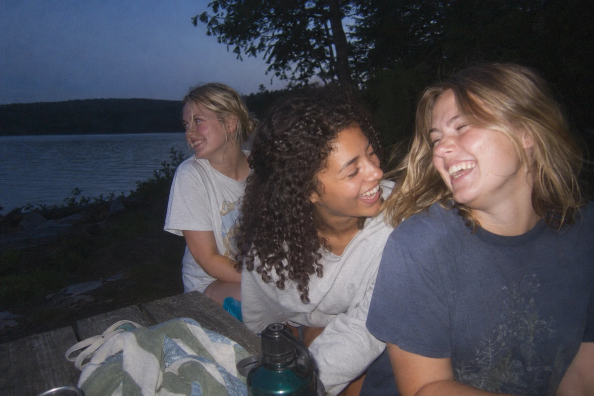 Drie vriendinnen lachen samen bij een meer.